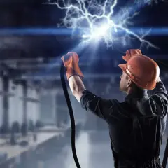 Elektryk w kasku i rękawicach trzyma przewody, z których wydobywa się potężne przepięcie elektryczne.