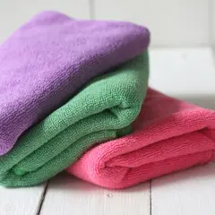 Drei bunte Mikrofasertücher, lila, grün und pink, liegen übereinander. Sie warten darauf, dass man sie zum putzlappen waschen benutzt.