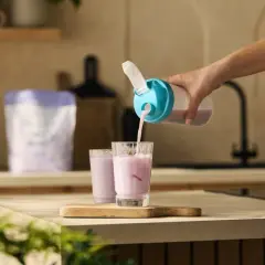 Eine Hand gießt einen rosa Proteinshake aus einem Shaker in ein Glas. So einfach ist es, was bewirken proteinshakes für die schnelle Nährstoffversorgung.