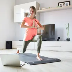 Kobieta ćwiczy jogę w domu, patrząc na laptopa.