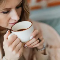 Kobieta z blond włosami pije kawę z kubka. Czy można pić kawę na czczo? Zastanawia się, delektując się aromatem.