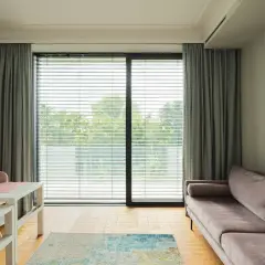 Elegancki karnisz do salonu z szarymi zasłonami, które tworzą przytulną atmosferę. Widoczny też wygodny, fioletowy narożnik.