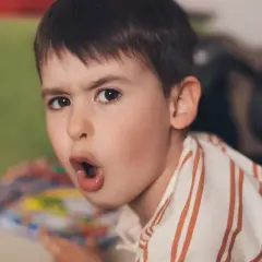 Chłopiec z otwartymi ustami i zdziwioną miną, w koszulce w paski.