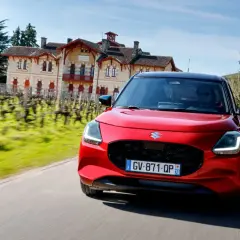 Czerwony Suzuki Swift pędzi drogą obok winnicy i zabytkowego domu.