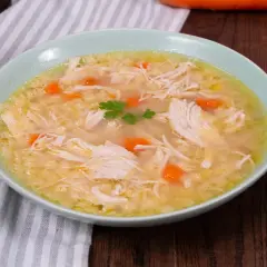 Un confortante brodo di pollo con pezzi di pollo sfilacciato, carote e un rametto di prezzemolo.