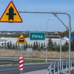 Uwaga na skrzyżowanie z drogą podporządkowaną i przejazd kolejowy. Znak "Elbląg" zaprasza do miasta.