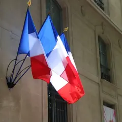 Trzy flagi Francji powiewają na tle kamiennej fasady budynku. Francuski to język urzędowy w wielu krajach, nie tylko w Europie.