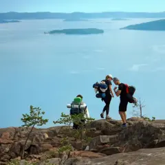 Vandrare med ryggsäckar njuter av utsikten över den blåa skärgården vid Höga kusten.