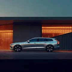 Srebrne Volvo V60 z hybrydowym silnikiem T8 zaparkowane przed nowoczesnym budynkiem z pomarańczowym podświetleniem.