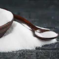 Biały proszek, prawdopodobnie erytrytol, w drewnianej miseczce i łyżce na ciemnym tle.