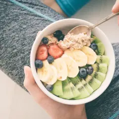 Miseczka owsianki z owocami: truskawkami, bananem, kiwi i borówkami. Idealne jedzenie po treningu.