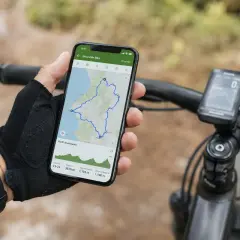 Mano con guante revisa en el móvil una ruta bici con perfil de elevación. Ciclocomputador en manillar.