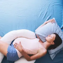 Mujer embarazada durmiendo de lado con almohadas de apoyo, una solución para como dormir con pubalgia y disfrutar del descanso.