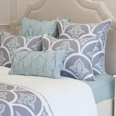 A bed with a tufted headboard, featuring large square pillows with a grey and white floral pattern, and smaller light blue accent pillows.