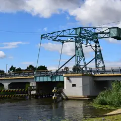 Most czterech pancernych, podnoszony most nad kanałem, z zieloną konstrukcją i błękitnym niebem.
