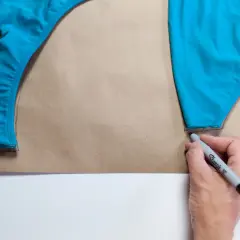 Tracing a blue swimsuit piece onto brown paper, a step in how to make a swimsuit.