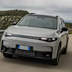 Leapmotor C10 REEV in grigio chiaro sfreccia su una strada panoramica, con un guidatore al volante.