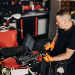 Mecánico con guantes naranjas usa un portátil para ver cómo se puede reprogramar una moto roja.