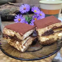 Dwa kawałki tiramisu, idealne ciasto do kawy, obok słoika z ziarnami kawy i fioletowych kwiatów.