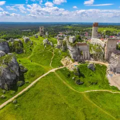 Ruiny zamków na wapiennych skałach w parku krajobrazowym Orlich Gniazd, otoczone zielonymi wzgórzami i lasami.