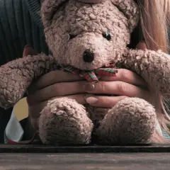 Dłoń obejmująca pluszowego misia na tle żółtym.