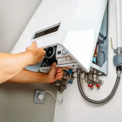 Tecnico che controlla la caldaia in blocco, con mani che aprono il pannello per ispezionare i componenti interni e le tubature.