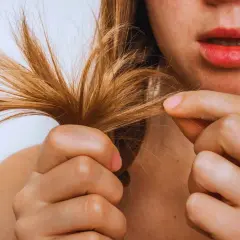 Una mujer examina su pelo seco, notando las puntas abiertas y la falta de brillo.