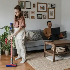 Kobieta sprząta mieszkanie odkurzaczem Dyson, podczas gdy mężczyzna pracuje na laptopie. Zastanawiasz się, który Dyson wybrać?