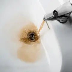 Acqua gialla dalla caldaia che scorre nel lavandino, creando un alone marrone.