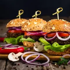 Trzy domowe burgery z bułkami pełnoziarnistymi, warzywami i dodatkami na drewnianej desce.