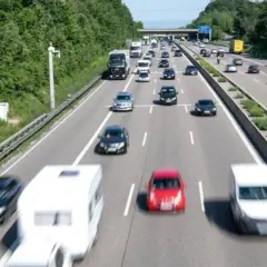 Autobahn mit vielen Autos und einem Wohnwagen. Ein Schild am Horizont deutet das ende autobahn schild an.