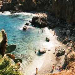 A secluded beach in Zingaro, Sicily, with crystal-clear turquoise water, rocky cliffs, and sunbathers enjoying the Mediterranean.