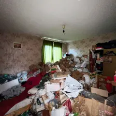 Un logement insalubre envahi par des montagnes de sacs et de détritus. La pièce est encombrée, rendant la circulation difficile.