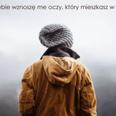Osoba w czapce i brązowej kurtce, patrząca w niebo. Cytat z Psalmu 134: "Do Ciebie wznoszę me oczy".