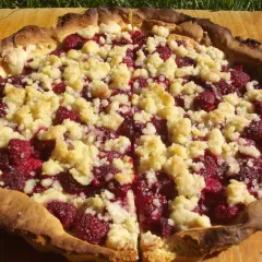 Pyszna tarta z malinami mrożonymi, posypana kruszonką, na drewnianej desce.