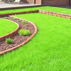 Curving wooden borders define a lush green lawn, showcasing creative landscape border ideas with a pebble-filled garden bed.