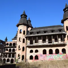 Niedokończony zamek w Łapalicach, z ceglanymi wieżami i łukowymi oknami, pokryty graffiti, pod błękitnym niebem.