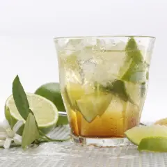Orzeźwiająca caipirinha przepis: drink z lodem, limonką i cukrem. Obok leżą świeże limonki i kwiatki.