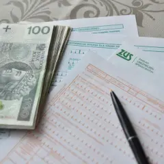 Stos papierów z ZUS, pieniądze i długopis sugerują, jak obliczana jest emerytura.
