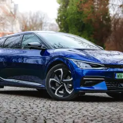 Niebieska Kia EV6 na testowej drodze, wśród drzew. Elegancki design i nowoczesne linie podkreślają jej elektryczny charakter.