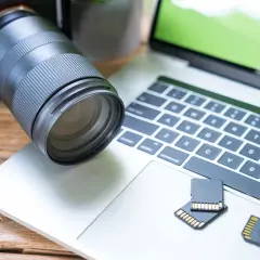 Aparat fotograficzny i karty pamięci leżą obok laptopa, gotowe do akcji. Dowiedz się, jak zgrać zdjęcia z aparatu na laptop.