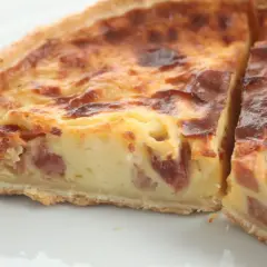 Un trozo de quiche de verduras con trocitos de bacon, horneado hasta dorarse.