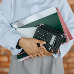 Osoba trzyma stos dokumentów i kalkulator. Idealne do usług fotograficznych, gdzie liczy się każdy szczegół, także VAT.