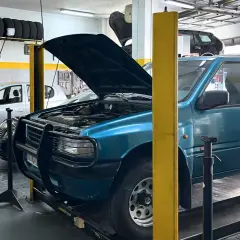 Taller mecánico con coches, neumáticos y herramientas. Se ven las copelas de un coche azul, parte del motor y la carrocería.