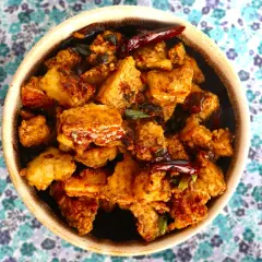 Crispy, golden-brown pieces of ice tofu are coated in a savory sauce with chili peppers and green onions, served in a bowl on a floral background.