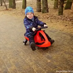 Uśmiechnięty chłopiec w czapce jedzie na czerwonym twistcarze. Od jakiego wieku można zacząć zabawę? Odpowiedź znajdziesz na blogu!