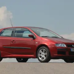 Czerwony Fiat Stilo 1.9 JTD z felgami aluminiowymi stoi na tle błękitnego nieba z chmurami.