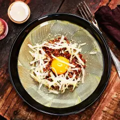 En läcker koreansk råbiff med en gul äggula i mitten, toppad med strimlad rättika och sesamfrön. Serveras på en vacker tallrik med en mörk servett och gaffel.