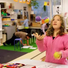 Mädchen jongliert mit Bällen im Klassenzimmer, während andere Kinder lernen. Ein Beispiel für bewegtes Lernen.