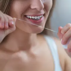 Uśmiechnięta kobieta nitkuje zęby. Pamiętaj, jak często nitkować zęby dla zdrowego uśmiechu.